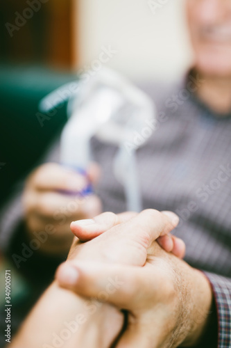 Holding hands for support with senior man  using medical equipment for inhalation with respiratory mask  nebulizer