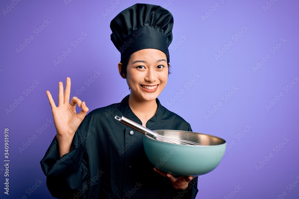 Young beautiful chinese chef woman wearing cooker uniform and hat using bowl and whisk doing ok sign with fingers, excellent symbol