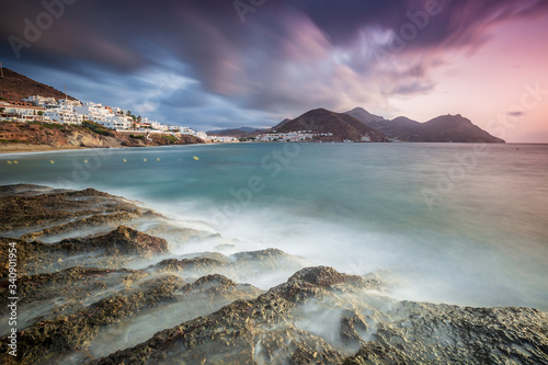 Landscape of the coast of the Natural Park of Cabo de Gata, Almería. Long exposure photograph with rock formation in the foreground and the town of San Jose in the background.