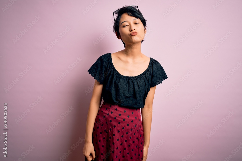 Young beautiful asian girl wearing casual dress standing over isolated pink background looking at the camera blowing a kiss on air being lovely and sexy. Love expression. Young beautiful asian girl wearing casual dress standing over isolated pink background looking at the camera blowing a kiss on air being lovely and sexy. Love expression.