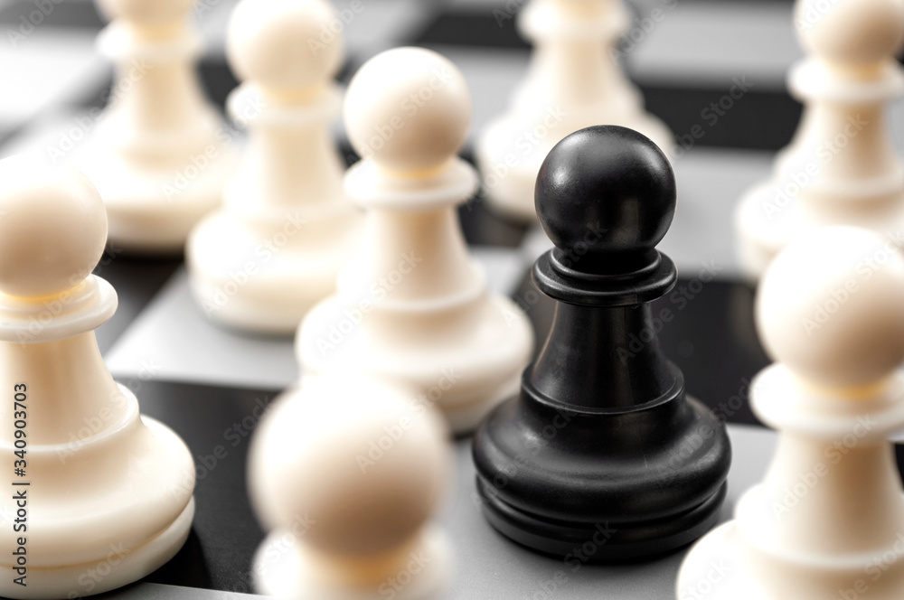 Leadership, diversity and individuality concept with black pawn surrounded by many white pawns on crowded chess board Leadership, diversity and individuality concept with black pawn surrounded by many white pawns on crowded chess board