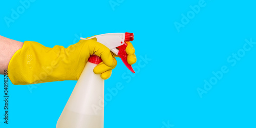 Hand in a yellow glove holds a spray with a dispenser. Bottle on a blue background. Sprayer for cleaning and disinfection of office and home. Side view, copy space.