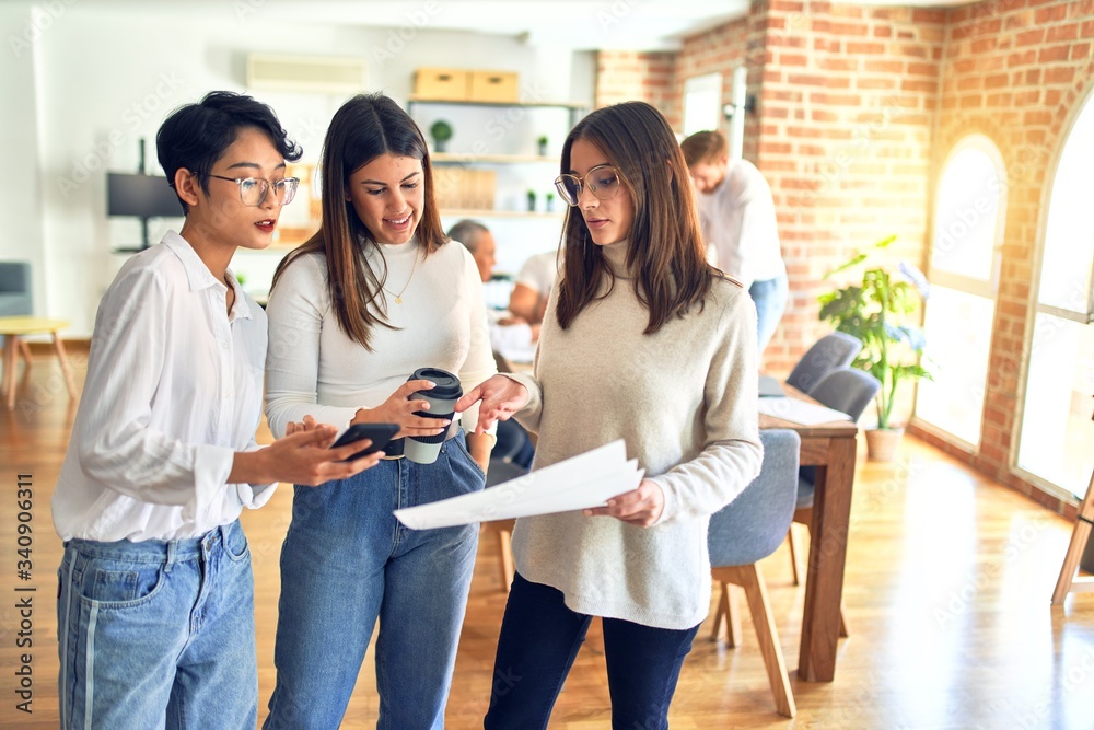 Beautiful businesswomen smiling happy. Standing with smile on face working together reading documents using smartphone at the office Beautiful businesswomen smiling happy. Standing with smile on face working together reading documents using smartphone at the office