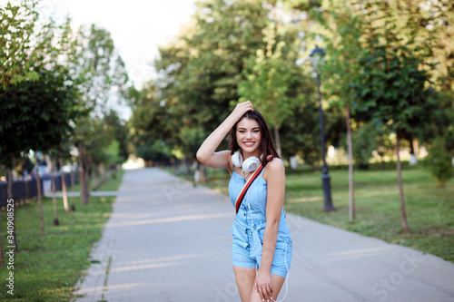 Cheerful woman is spending time outdoors in the park alley in summer. Woman is wearing blue rompersuit. © Natalia