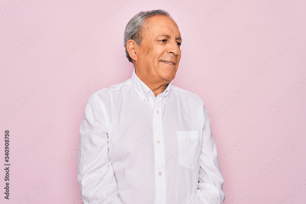 Senior handsome grey-haired man wearing elegant shirt over isolated pink background looking away to side with smile on face, natural expression. Laughing confident. Senior handsome grey-haired man wearing elegant shirt over isolated pink background looking away to side with smile on face, natural expression. Laughing confident.