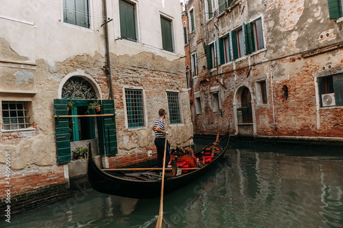 The gondolier controls a beautiful gondola sailing through a narrow channel where the water is green | VENICE, ITALY - 16 SEPTEMBER 2018. 
