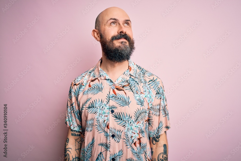 Handsome bald man with beard and tattoo wearing casual floral shirt over pink background smiling looking to the side and staring away thinking. Handsome bald man with beard and tattoo wearing casual floral shirt over pink background smiling looking to the side and staring away thinking.