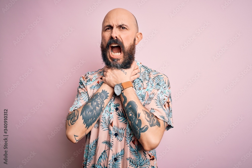Handsome bald man with beard and tattoo wearing casual floral shirt over pink background shouting suffocate because painful strangle. Health problem. Asphyxiate and suicide concept.