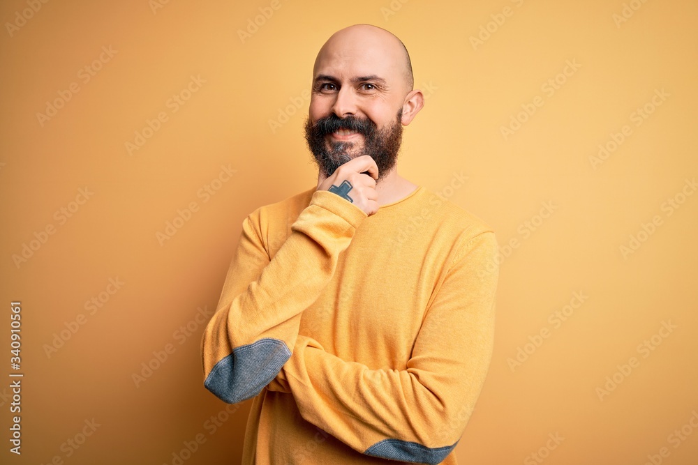 Handsome bald man with beard wearing casual sweater standing over yellow background looking confident at the camera smiling with crossed arms and hand raised on chin. Thinking positive. Handsome bald man with beard wearing casual sweater standing over yellow background looking confident at the camera smiling with crossed arms and hand raised on chin. Thinking positive.
