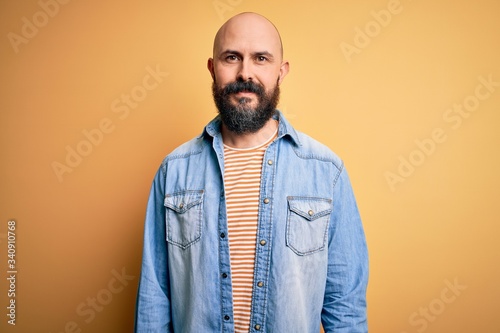 Handsome bald man with beard wearing casual denim jacket and striped t-shirt with a happy and cool smile on face. Lucky person.