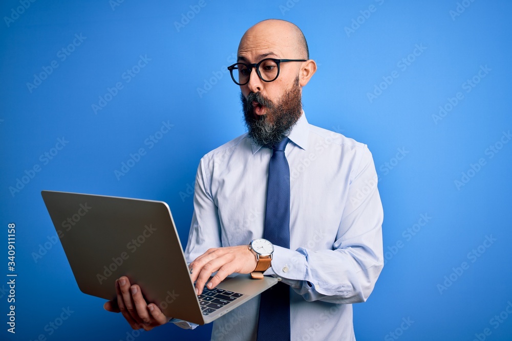 Handsome bald business man with beard working using laptop over blue background scared in shock with a surprise face, afraid and excited with fear expression Handsome bald business man with beard working using laptop over blue background scared in shock with a surprise face, afraid and excited with fear expression