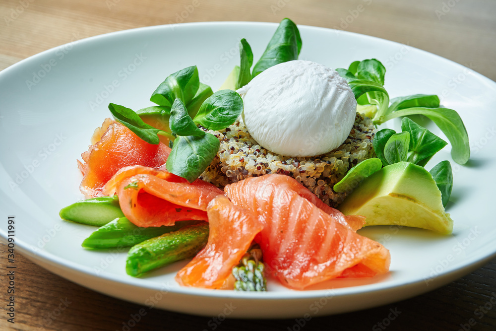 Tasty and healthy continental breakfast - quinoa with benedict eggs, spinach, avocado, salted salmon and asparagus in white bowl. Wooden background Tasty and healthy continental breakfast - quinoa with benedict eggs, spinach, avocado, salted salmon and asparagus in white bowl. Wooden background