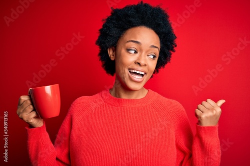 African American afro woman with curly hair drinking cup of coffee over red background pointing and showing with thumb up to the side with happy face smiling