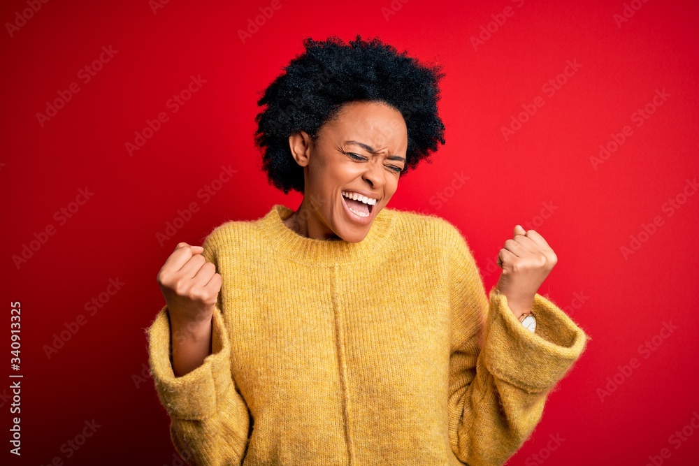 Young beautiful African American afro woman with curly hair wearing casual yellow sweater very happy and excited doing winner gesture with arms raised, smiling and screaming for success. Celebration Young beautiful African American afro woman with curly hair wearing casual yellow sweater very happy and excited doing winner gesture with arms raised, smiling and screaming for success. Celebration