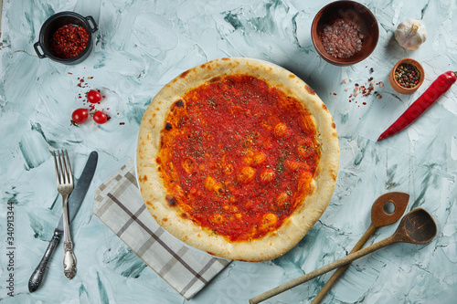 Freshly baked crispy pizza with marinara sauce on a gray background in a composition with ingredients and kitchen utensils