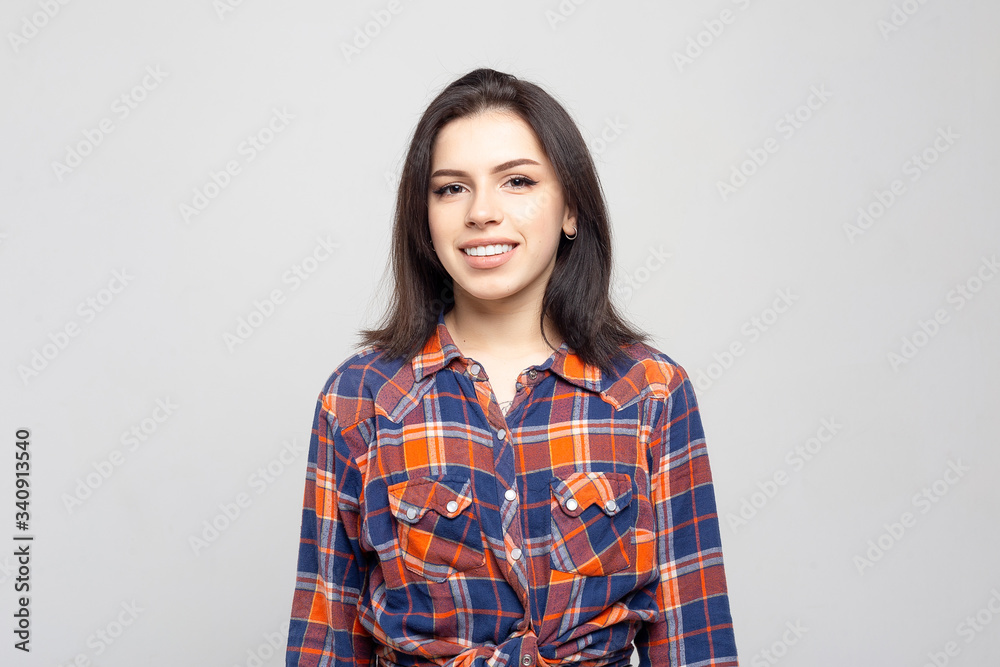 Beautiful young woman portrait. Portrait of a beautiful smiling brunette in a plaid shirt on a white-gray Beautiful young woman portrait. Portrait of a beautiful smiling brunette in a plaid shirt on a white-gray