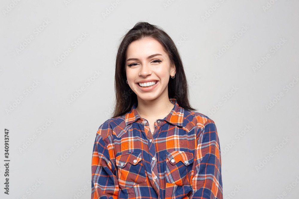 Beautiful young woman portrait. Portrait of a beautiful smiling brunette in a plaid shirt on a white-gray Beautiful young woman portrait. Portrait of a beautiful smiling brunette in a plaid shirt on a white-gray