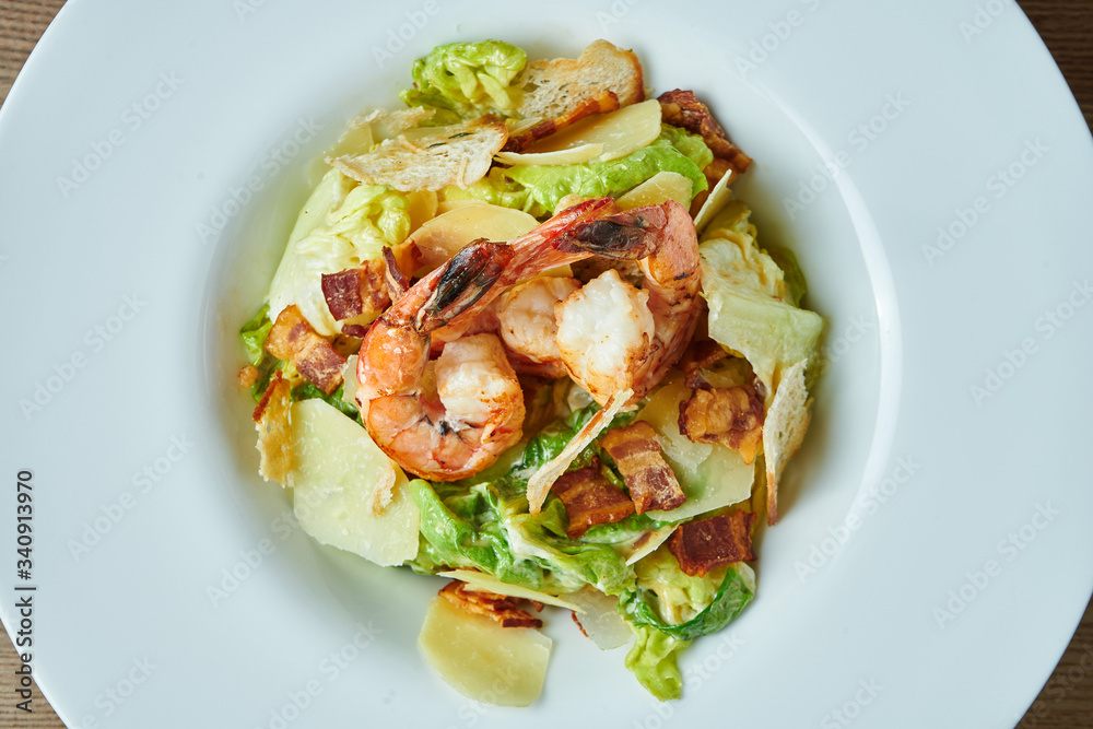 Appetizing Caesar with prawns, bacon, lettuce, parmesan and croutons in a white bowl. Seafood salad. Close up view