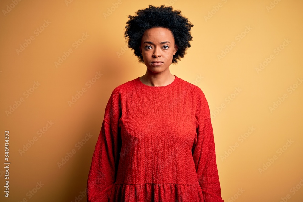 Young beautiful African American afro woman with curly hair wearing casual sweater with serious expression on face. Simple and natural looking at the camera.