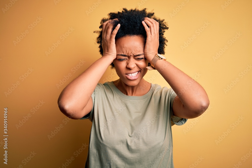 Young beautiful African American afro woman with curly hair wearing casual t-shirt suffering from headache desperate and stressed because pain and migraine. Hands on head.