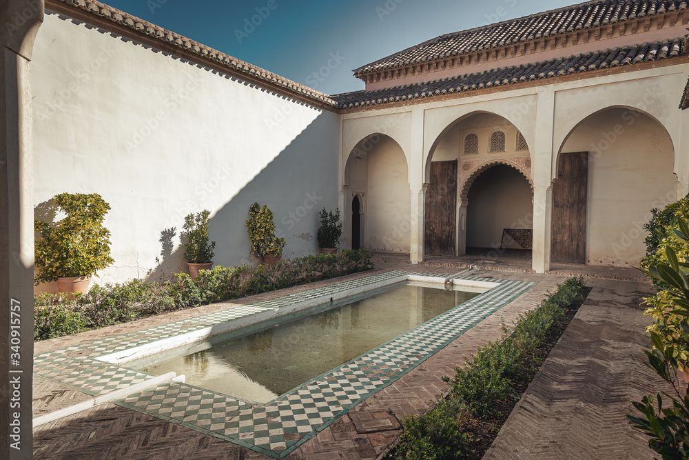 Obraz premium Alcazaba interior courtyard with pool and covered walkway and columns and arches from moorish islamic architecture in Malaga Spain with plants, daylight with shadows.