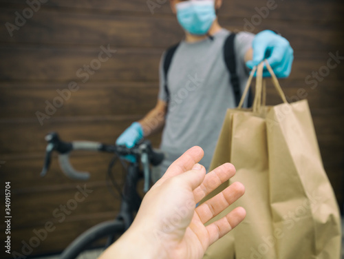 The courier on the bicycle is delivering the paper bag with order to the person