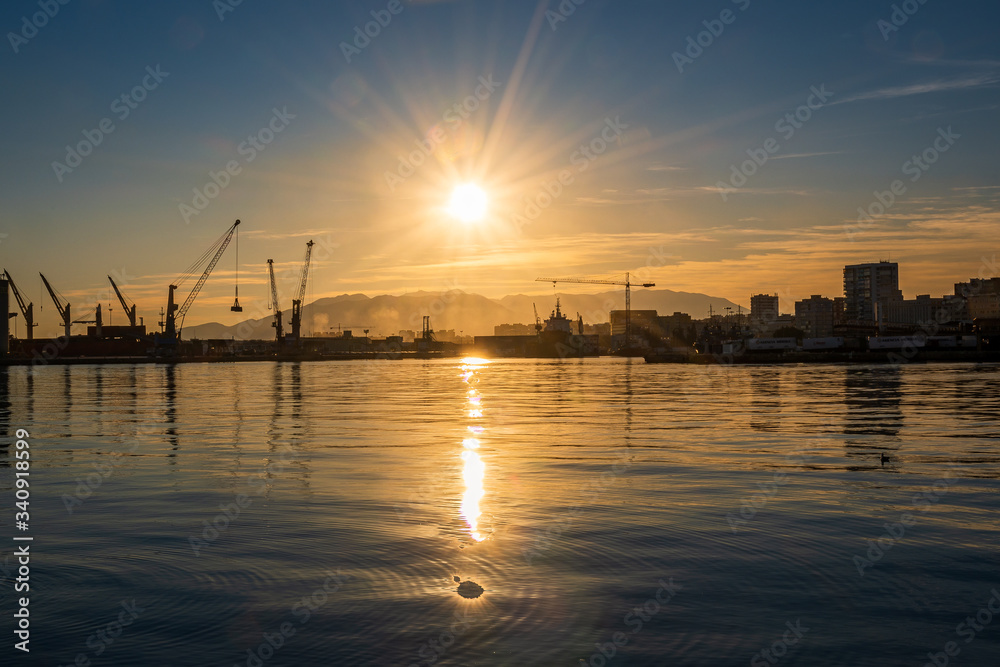 Backlit sunset in the port of Malaga with cranes and the sun reflecting in the sea water.