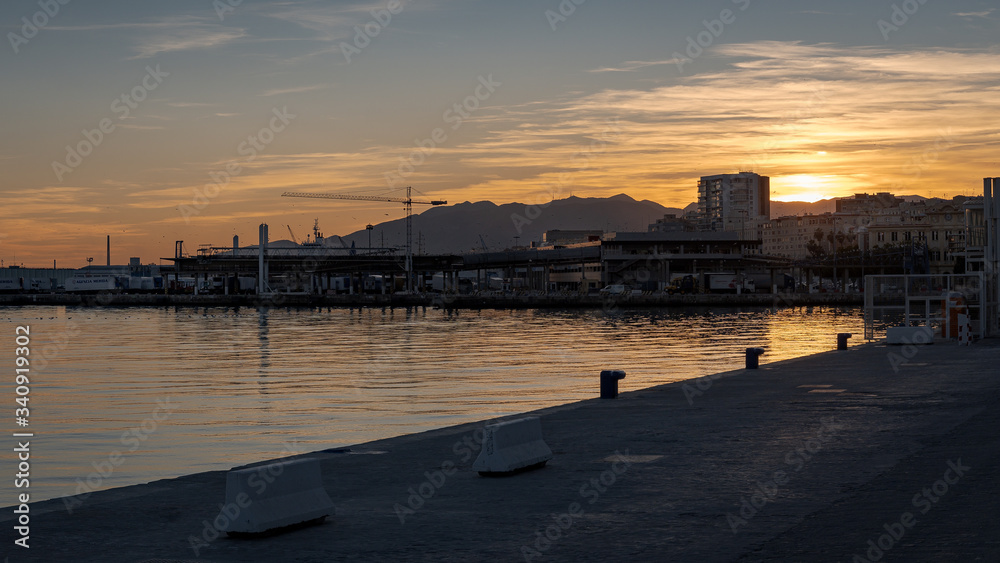 Sunset on the Port of Malaga Spain. Docks with cranes silhouette with the sun setting behind the hills in backlight.