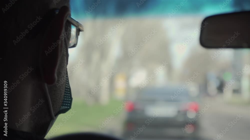 Man in protective medical mask drives car through city during outbreak of dangerous disease around world. Male in vehicle on town Man in protective medical mask drives car through city during outbreak of dangerous disease around world. Male in vehicle on town
