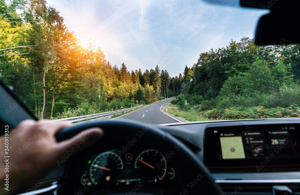 Hands of car driver on steering wheel, fast driving car at spring day on a country road, having fun driving the empty highway on tour journey - POV, first person view shot
