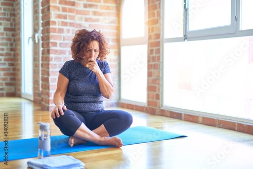 Middle age beautiful sportswoman wearing sportswear sitting on mat practicing yoga at home feeling unwell and coughing as symptom for cold or bronchitis. Healthcare concept.