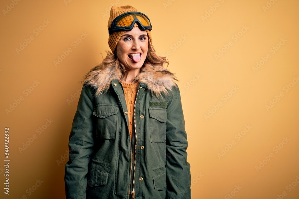 Middle age beautiful blonde skier woman wearing snow sportwear and ski goggles sticking tongue out happy with funny expression. Emotion concept. Middle age beautiful blonde skier woman wearing snow sportwear and ski goggles sticking tongue out happy with funny expression. Emotion concept.