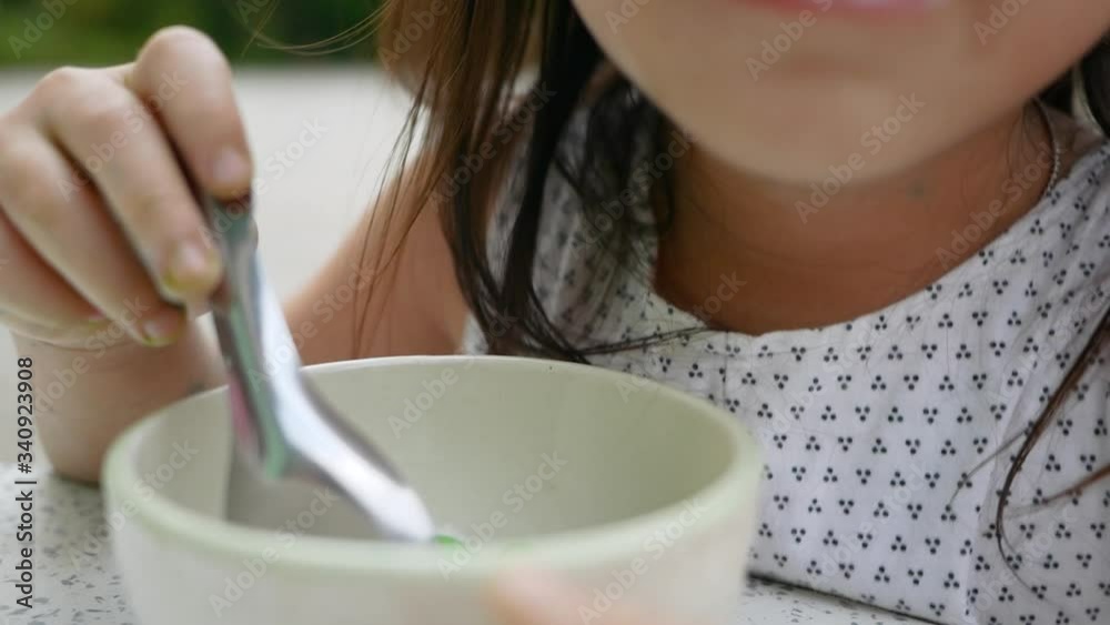 Cute little Asian child girl eating thai dumplings dessert or Bualoy with coconut milk in small bowl on marble table in front of the house. Cute little Asian child girl eating thai dumplings dessert or Bualoy with coconut milk in small bowl on marble table in front of the house.