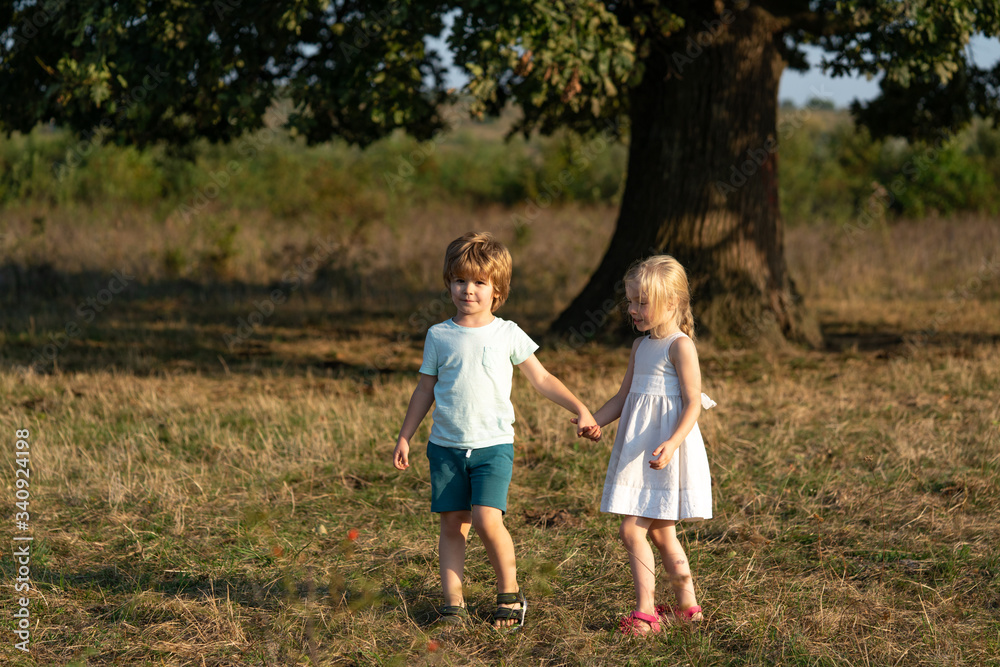 Happy little couple holding hands on field background. Children holding hands. Summer in love.