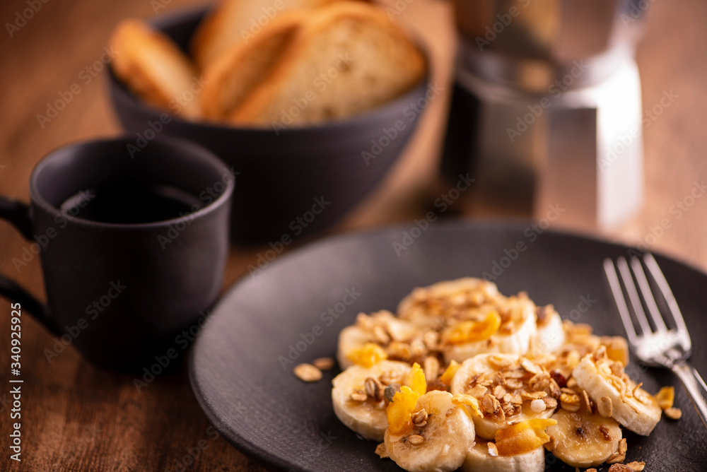 plate with sliced banana with granola, candied fruit and honey, toast and a cup of coffee plate with sliced banana with granola, candied fruit and honey, toast and a cup of coffee
