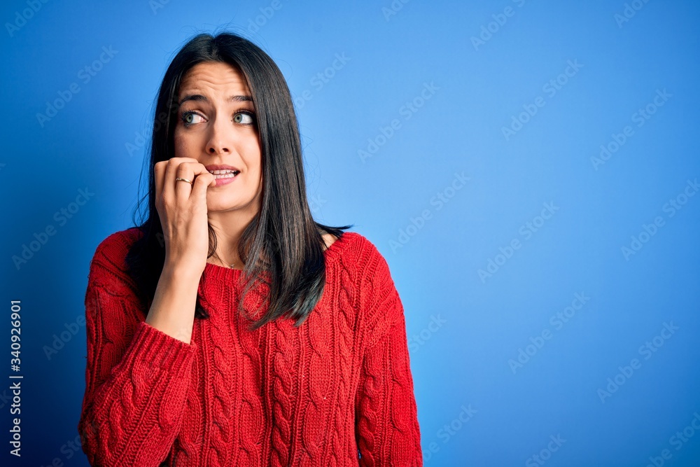 Young brunette woman with blue eyes wearing red casual sweater over isolated background looking stressed and nervous with hands on mouth biting nails. Anxiety problem. Young brunette woman with blue eyes wearing red casual sweater over isolated background looking stressed and nervous with hands on mouth biting nails. Anxiety problem.