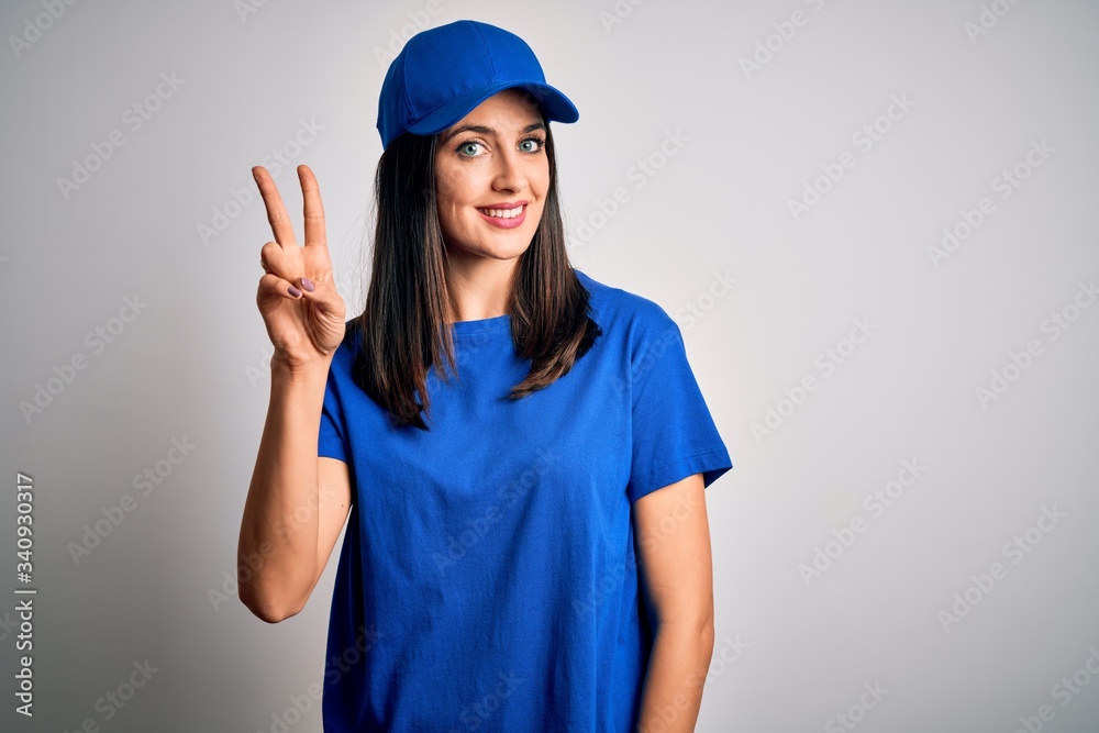 Young delivery woman with blue eyes wearing cap standing over blue background showing and pointing up with fingers number two while smiling confident and happy. Young delivery woman with blue eyes wearing cap standing over blue background showing and pointing up with fingers number two while smiling confident and happy.