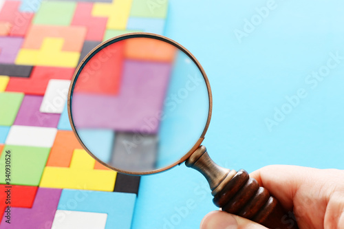 concept image of magnifying glass over puzzle background. finding the right piece.