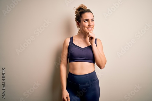 Young beautiful blonde sportswoman doing sport wearing sportswear over white background with hand on chin thinking about question, pensive expression. Smiling with thoughtful face. Doubt concept. © Krakenimages.com