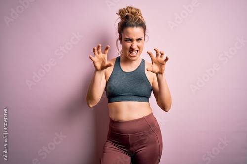 Young beautiful blonde sportswoman doing sport wearing sportswear over pink background smiling funny doing claw gesture as cat, aggressive and sexy expression © Krakenimages.com