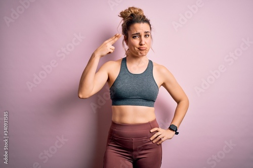 Young beautiful blonde sportswoman doing sport wearing sportswear over pink background Shooting and killing oneself pointing hand and fingers to head like gun, suicide gesture. © Krakenimages.com
