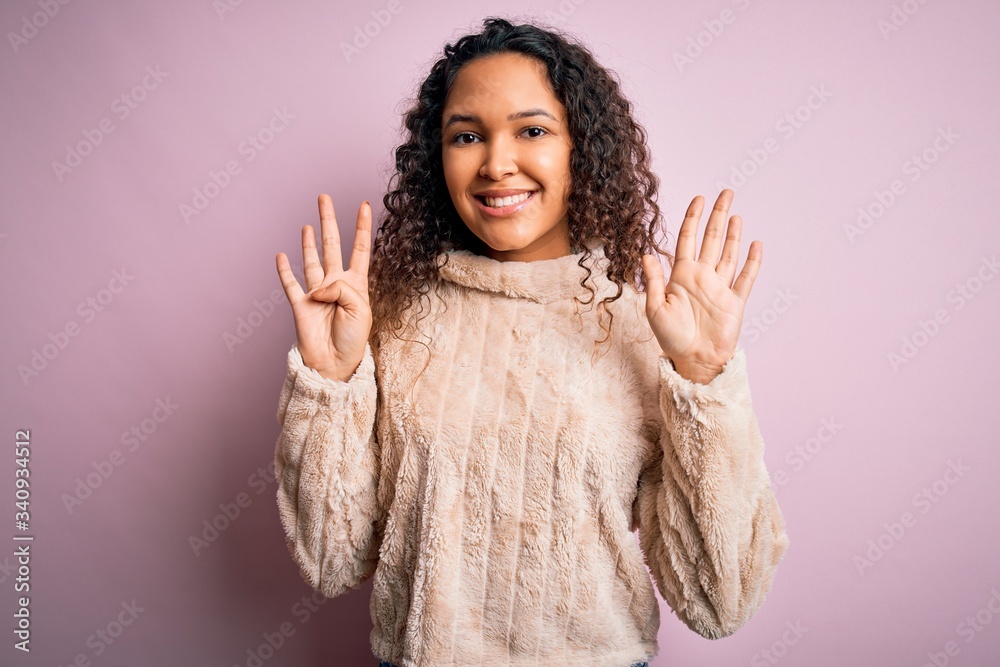 Young beautiful woman with curly hair wearing casual sweater standing over pink background showing and pointing up with fingers number nine while smiling confident and happy. Young beautiful woman with curly hair wearing casual sweater standing over pink background showing and pointing up with fingers number nine while smiling confident and happy.