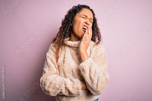 Young beautiful woman with curly hair wearing casual sweater standing over pink background bored yawning tired covering mouth with hand. Restless and sleepiness.