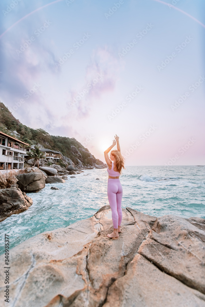 Pregnant woman practices yoga, standing in vrksasana position on the beach, on the rocks. Hands of girl in a pose meditating. Serenity practicing at sunrise, meditation. Woman in pink-purple tracksuit Pregnant woman practices yoga, standing in vrksasana position on the beach, on the rocks. Hands of girl in a pose meditating. Serenity practicing at sunrise, meditation. Woman in pink-purple tracksuit