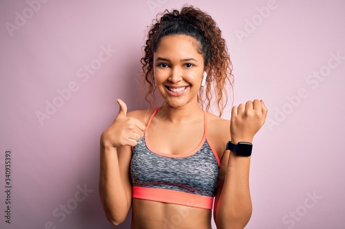 Beautiful sportswoman with curly hair doing sport wearing sportswear using smartwatch happy with big smile doing ok sign, thumb up with fingers, excellent sign © Krakenimages.com