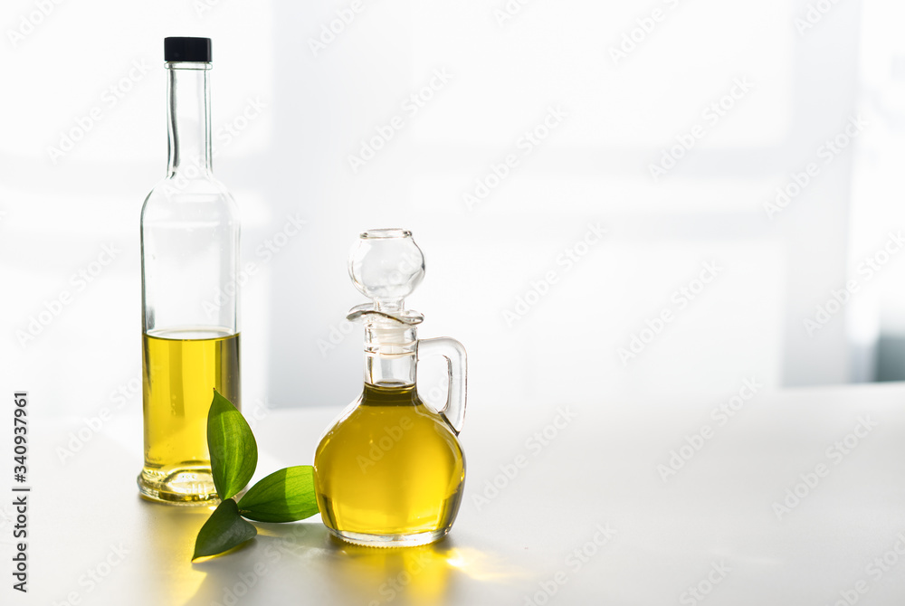 against the window, olive oil in a decanter and in a glass bottle, with a green leaf against the window, olive oil in a decanter and in a glass bottle, with a green leaf