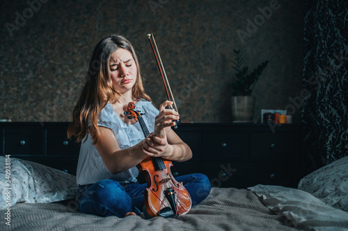 A young brunette girl injured her wrist while playing the violin. A girl sits on a bed in her room and holds a sore wrist with her hand