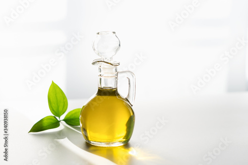 against the window, olive oil in a decanter on a white background with a green leaf