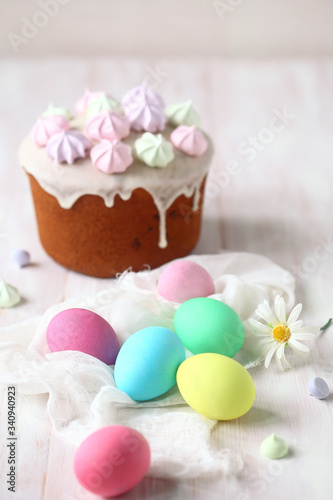 Kulich Russian Easter Cake with raisins, topped with icing glaze and decorated with colored meringue cookies, on white wooden table.