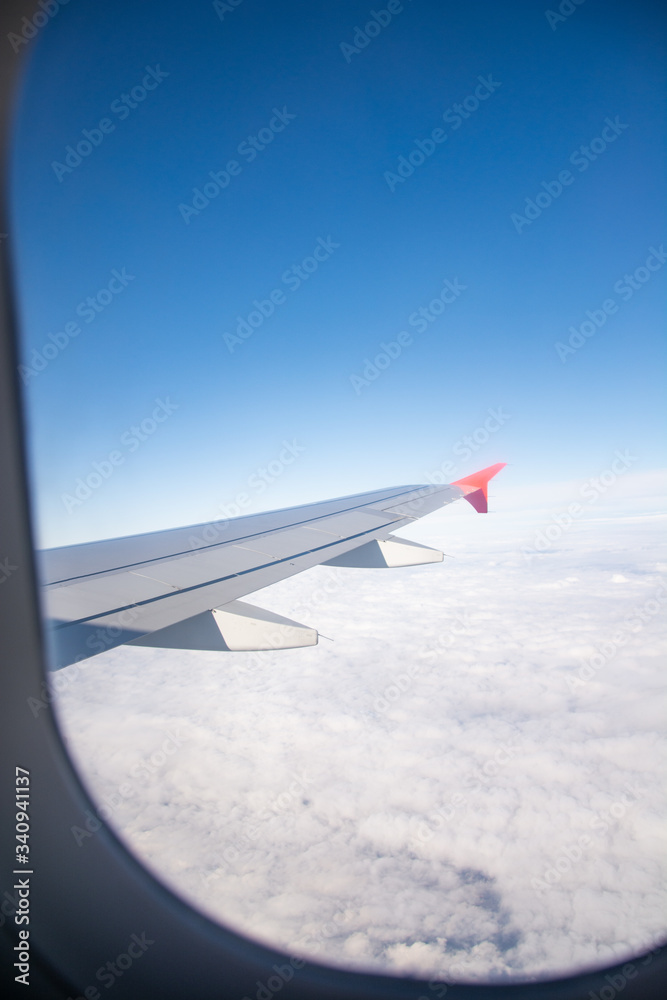 Fototapeta premium Airplane wing and clouds are visible from the porthole.